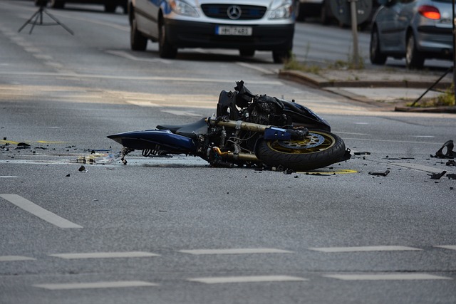 An image capturing the aftermath of Don Dodge's motorcycle accident: a twisted, mangled bike lying on the pavement, shattered windscreen, scattered broken parts, and a concerned crowd gathering around